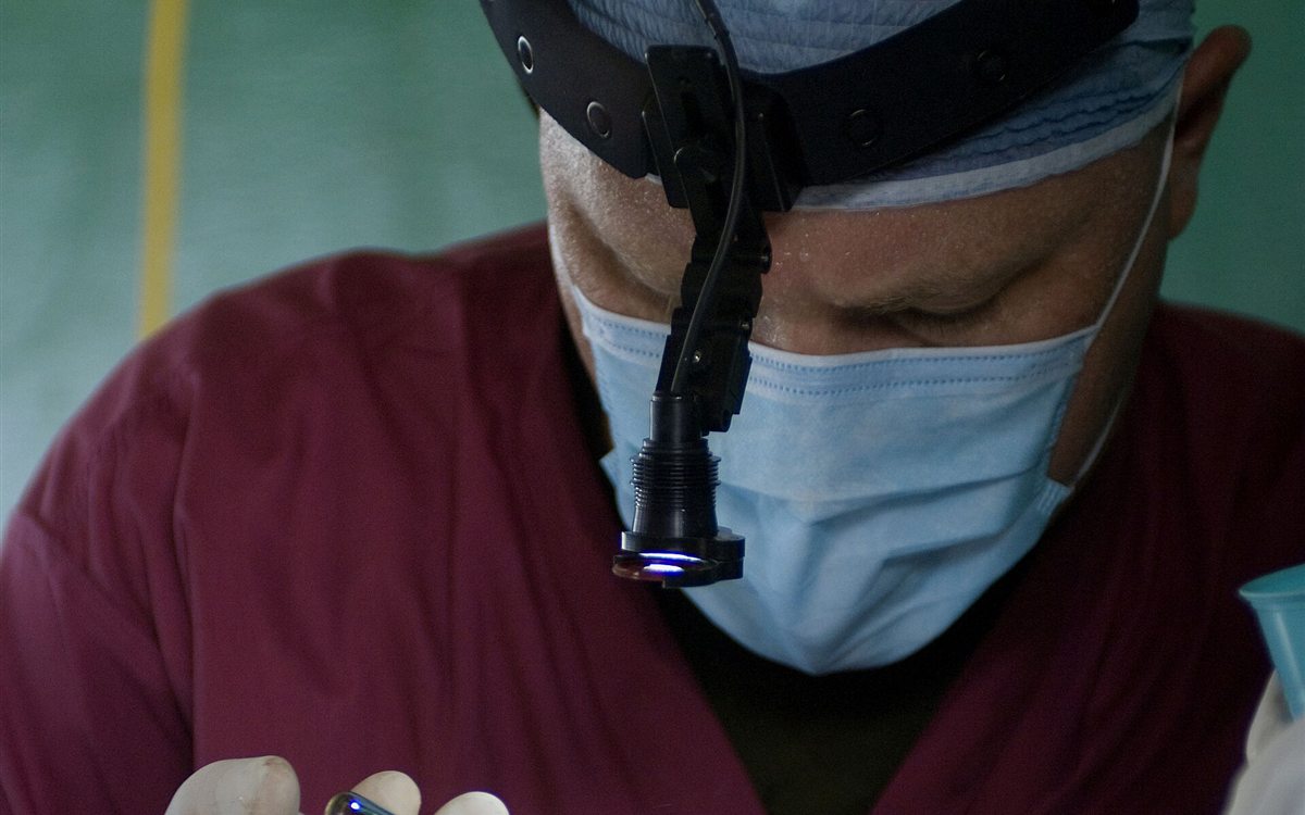 Dokter gigi bermasker dengan lampu kepala saat tindakan cabut gigi